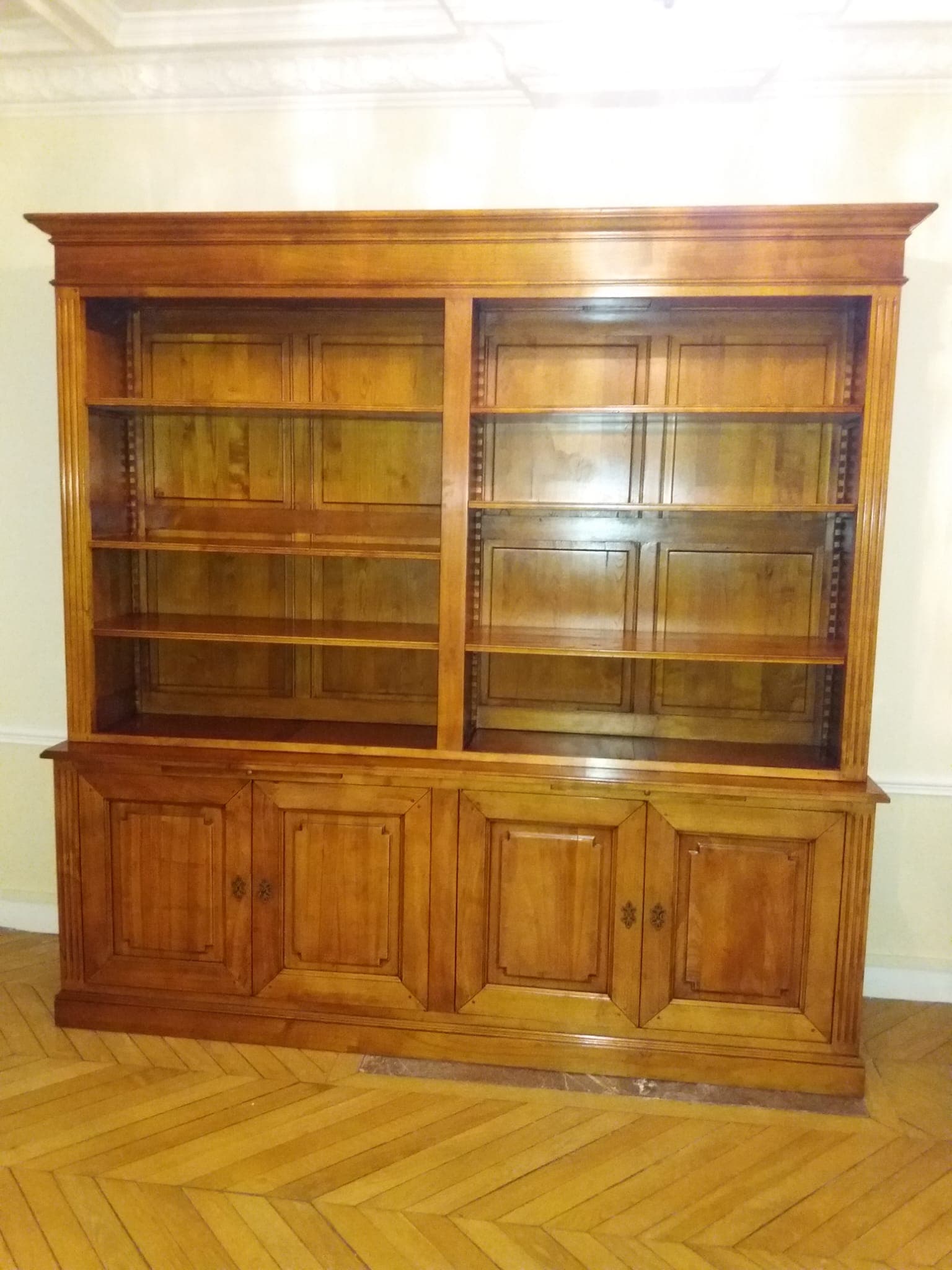 Bibliothèque deux corps en merisier massif : deux travées de tablettes réglables sur crémaillères, fonds menuisés à panneaux, quatre portes à panneaux moulurés à angles rentrants et montants cannelés