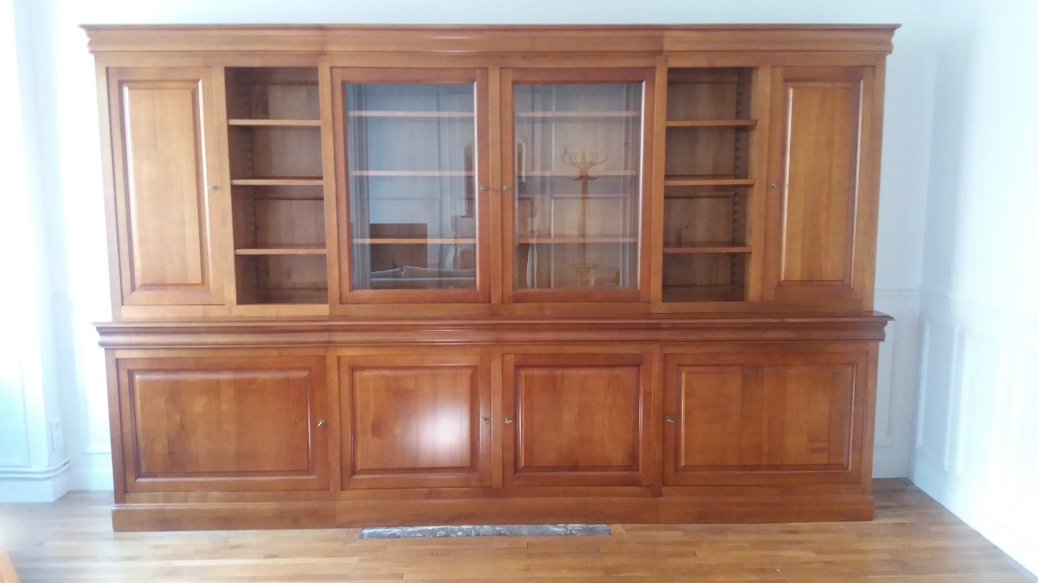Bibliothèque deux corps de 3 mètres en merisier massif : vitrine centrale à deux portes en ressaut, deux travées de rayonnages ouverts, portes pleines à panneaux aux extrémités et quatre portes en partie basse