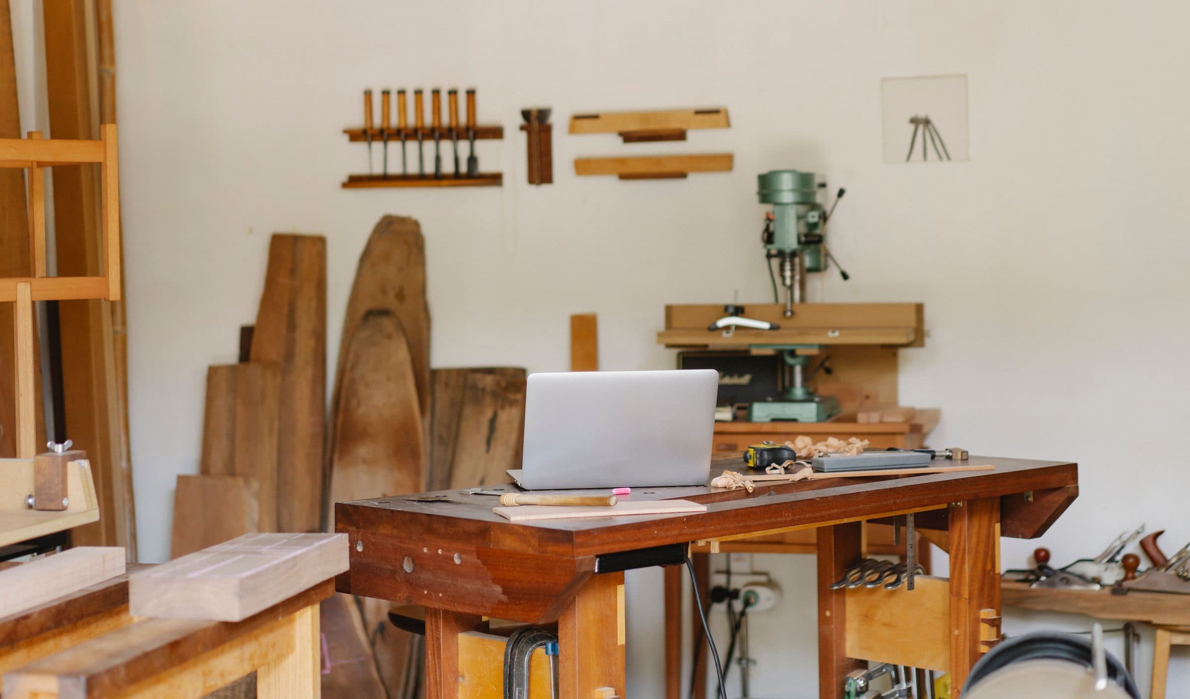Établi de menuisier en bois massif, ciseaux à bois alignés sur leur râtelier et perceuse à colonne dans l’atelier