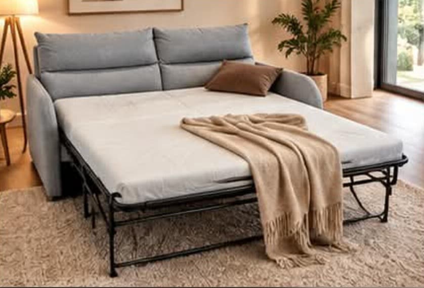 Le même canapé en tissu gris ouvert en lit sur son sommier métallique, matelas garni d’un plaid