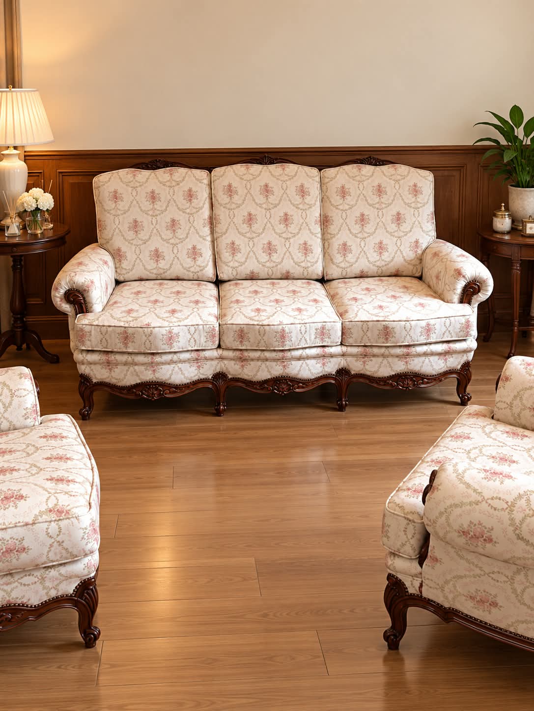 Canapé trois places Louis XV garni d’un tissu ivoire à bouquets de roses, ceinture chantournée sculptée de coquilles, pieds cambrés, avec deux fauteuils assortis au premier plan