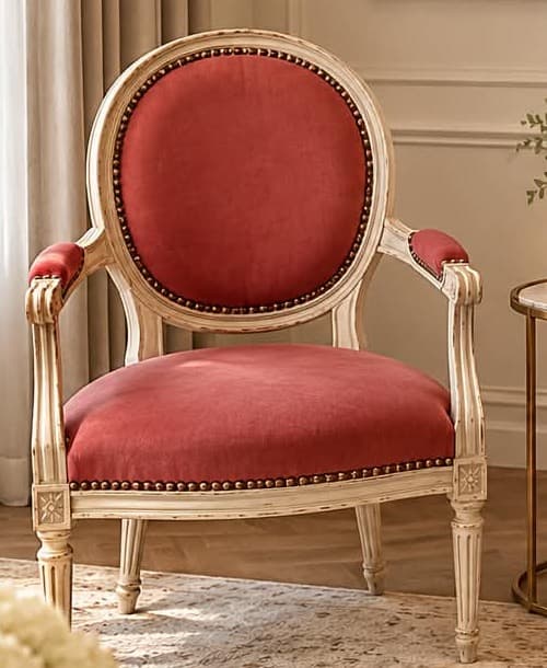 Fauteuil cabriolet Louis XVI à dossier médaillon, bois patiné blanc aux arêtes frottées, garni d’un velours vieux rose bordé de clous de laiton, manchettes garnies et pieds fuselés cannelés