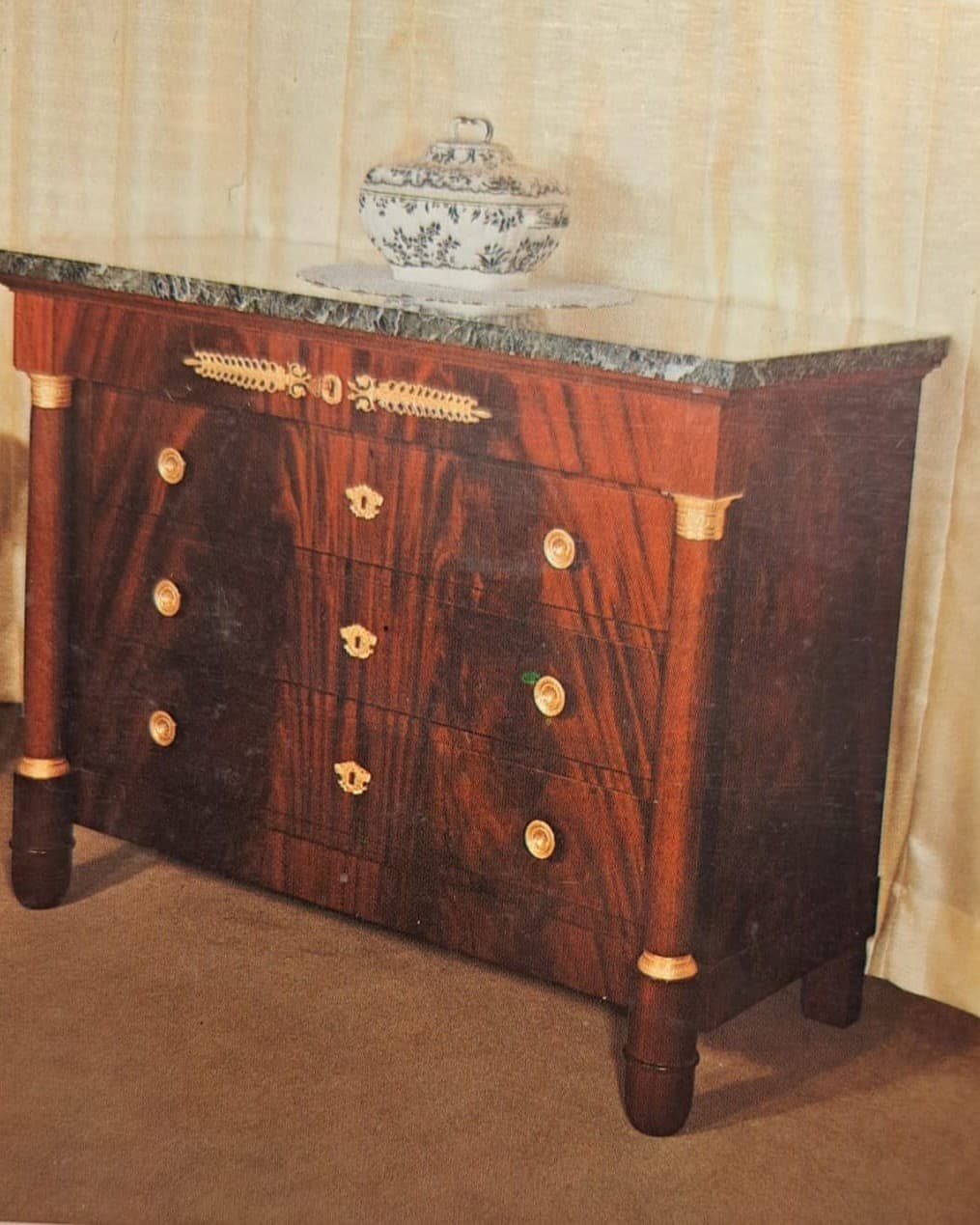 Commode de style Empire à placage flammé : quatre tiroirs, applique de bronze doré à palmettes sur le tiroir de frise, colonnes détachées à chapiteaux de bronze, dessus de marbre et pieds toupie