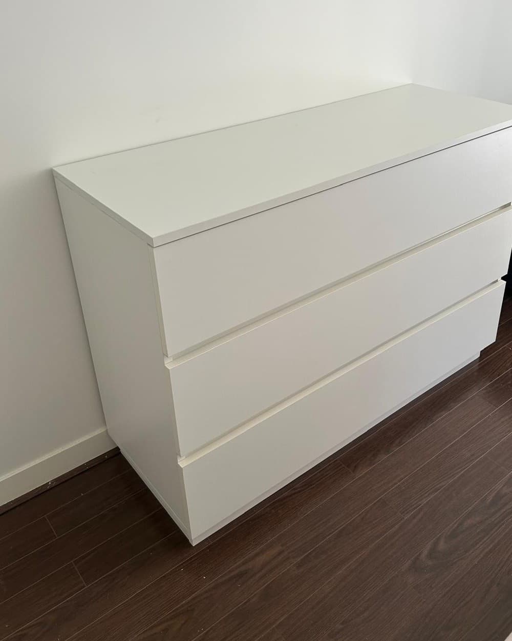 Commode contemporaine laquée blanc mat à trois grands tiroirs sans poignée, ouverts par le chant, plateau légèrement débordant et socle en retrait