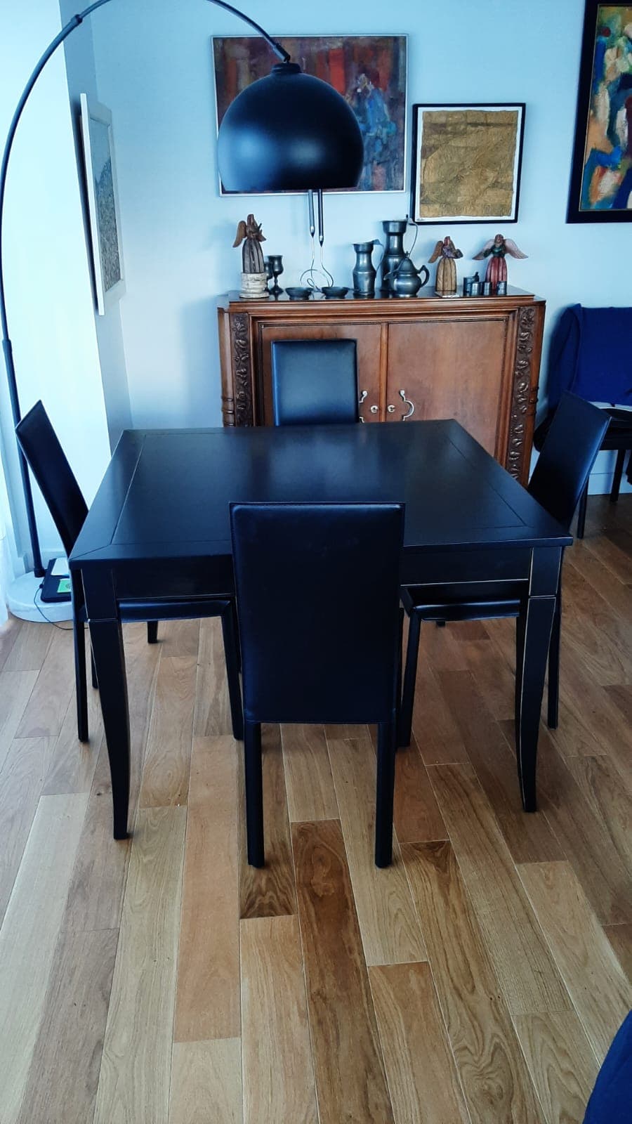 Table de repas carrée laquée noir à pieds sabre évasés, plateau encadré d’une moulure en réserve, entourée de chaises noires