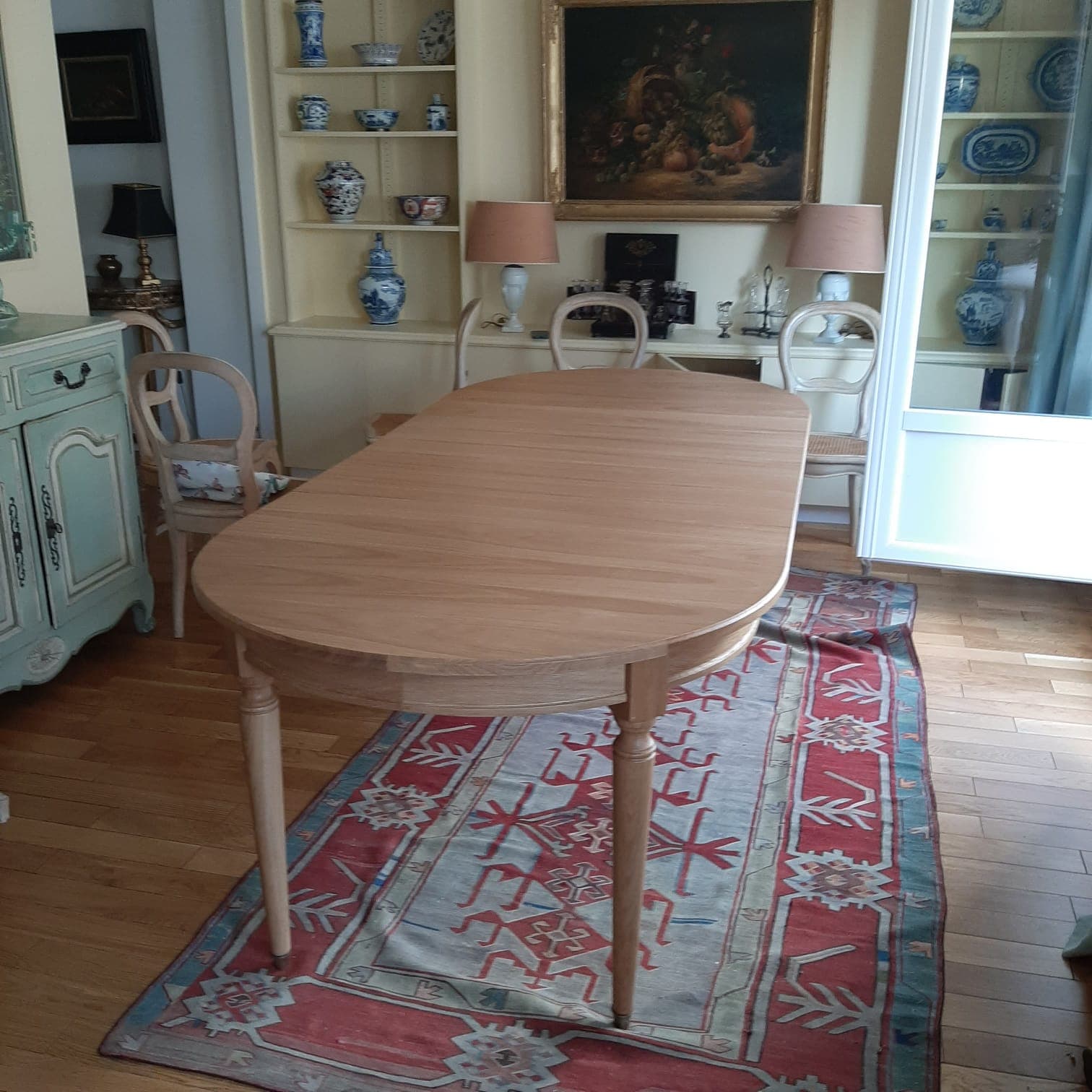 Table ovale en chêne massif huilé à pieds fuselés et roulettes laiton, dans une salle à manger parisienne ornée de faïences bleues